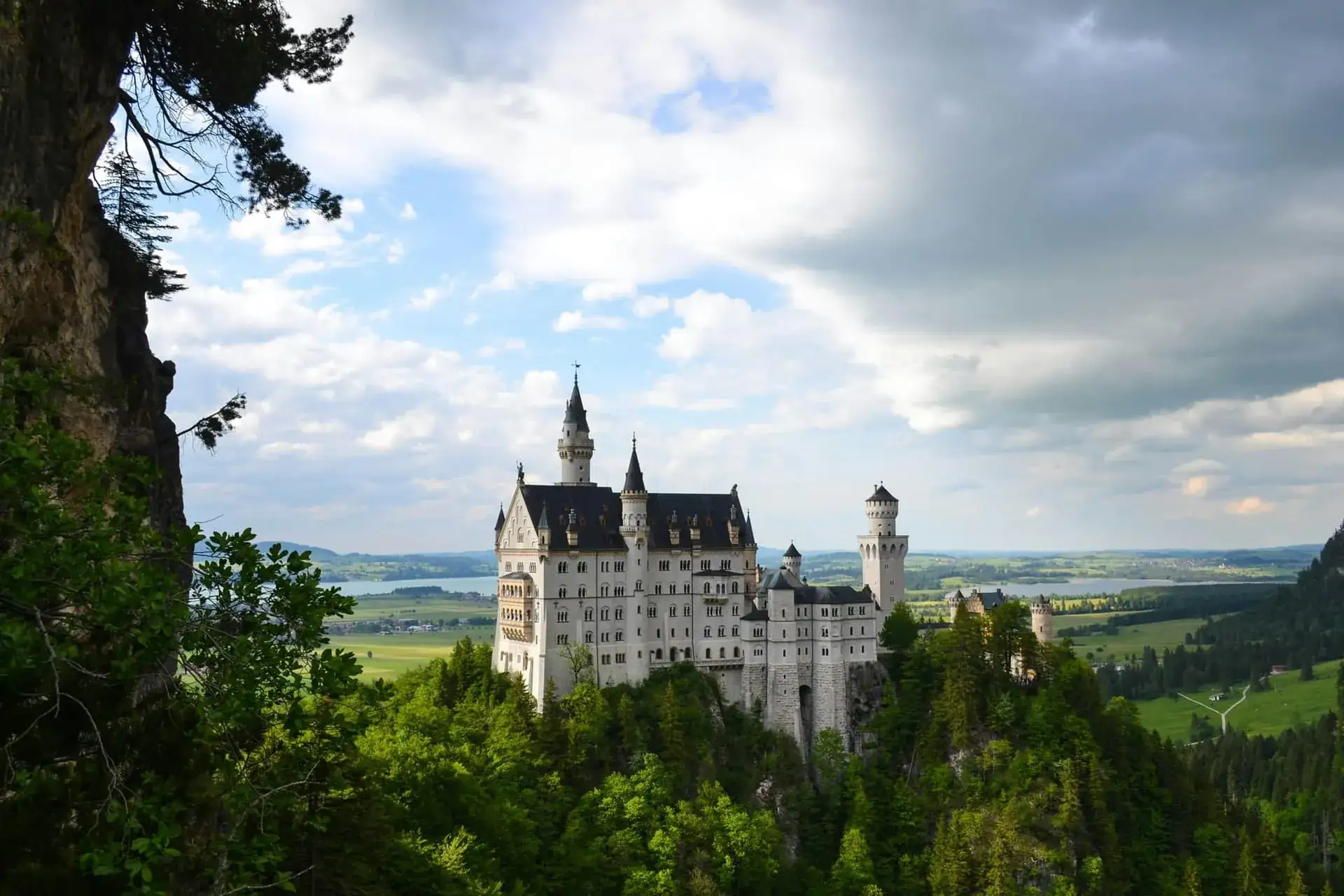 Le château de Neuschwanstein sur son éperon boisé, lacs et plaine bavaroise en arrière-plan