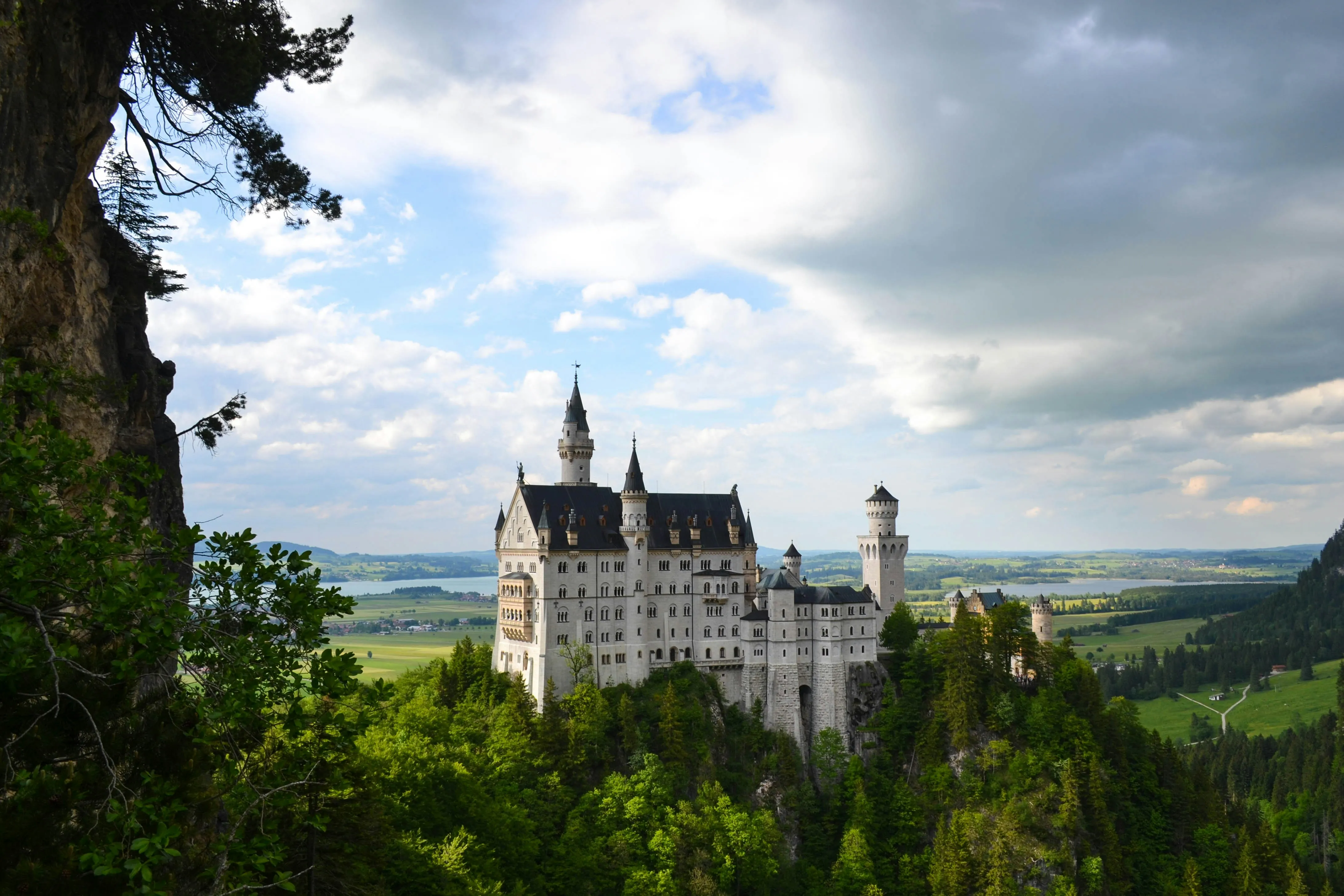 Le château de Neuschwanstein sur son éperon boisé, lacs et plaine bavaroise en arrière-plan