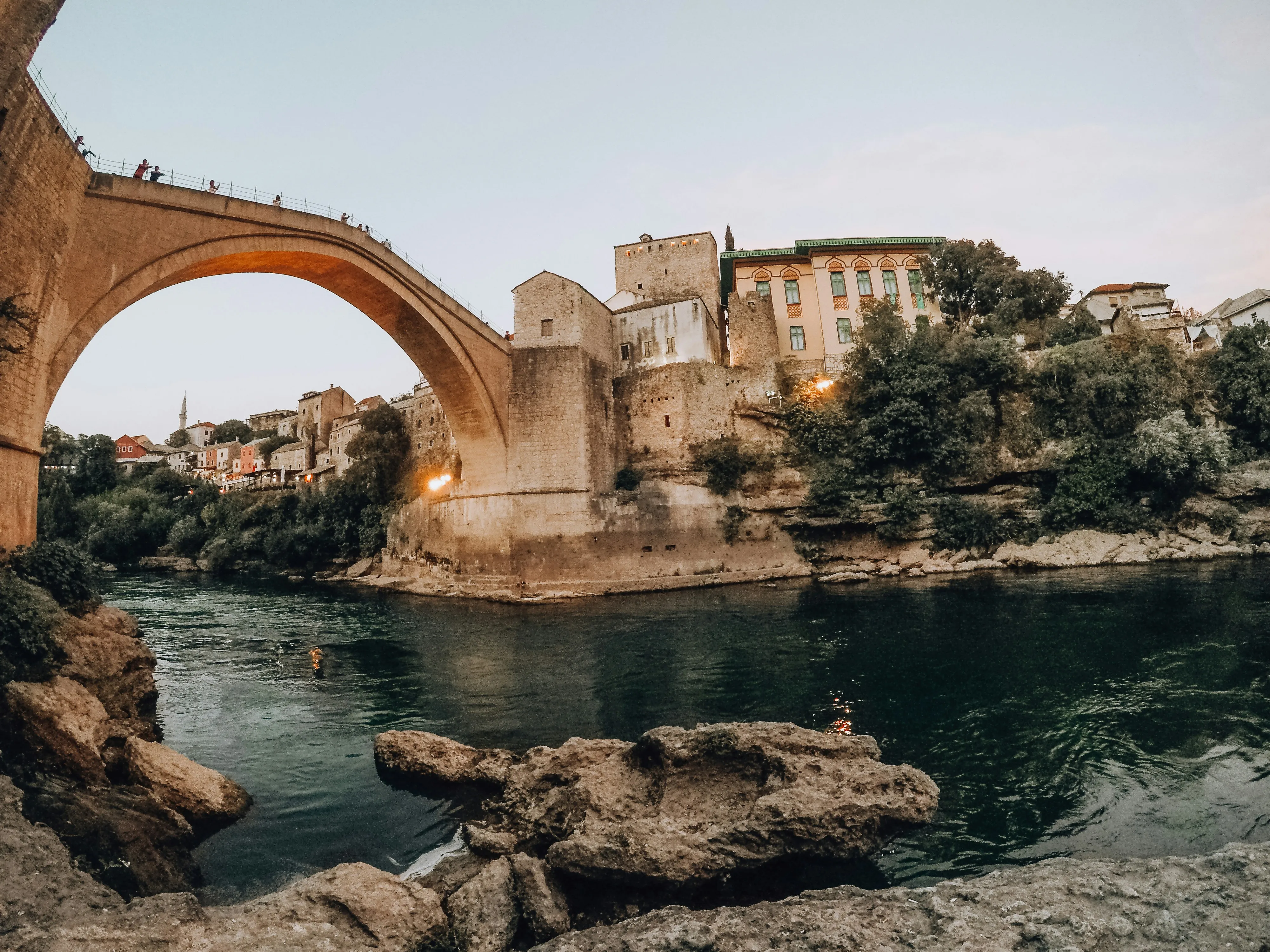 Le vieux pont de Mostar enjambant la Neretva au crépuscule, minaret et maisons de pierre en arrière-plan