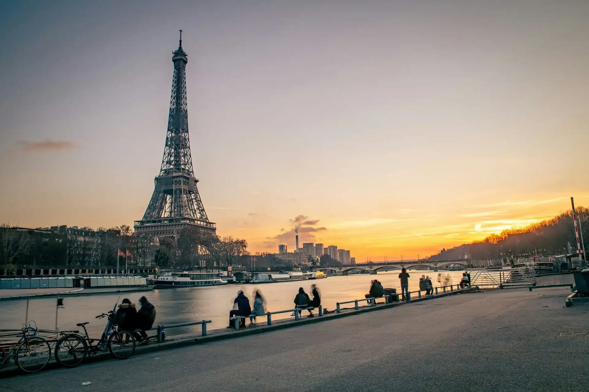 La tour Eiffel au coucher du soleil depuis les quais de Seine, promeneurs assis face au fleuve