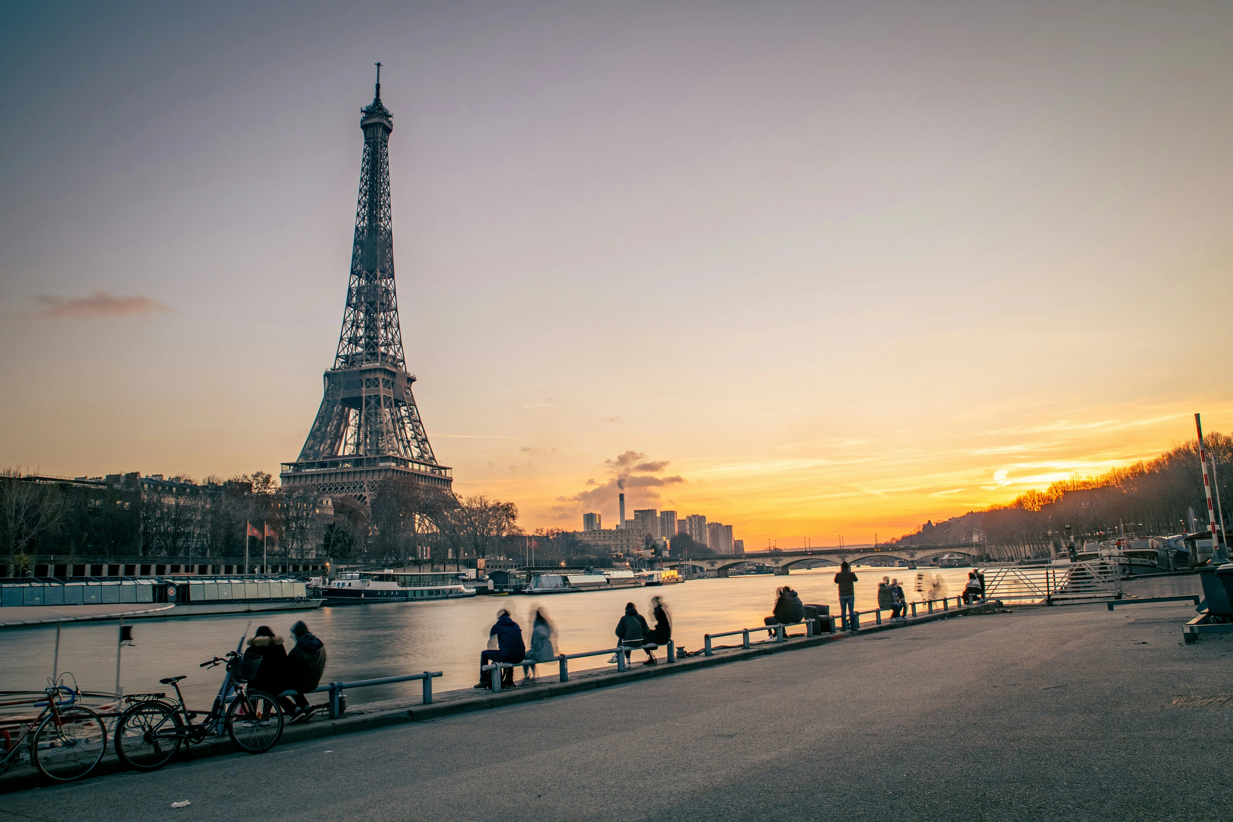 La tour Eiffel au coucher du soleil depuis les quais de Seine, promeneurs assis face au fleuve