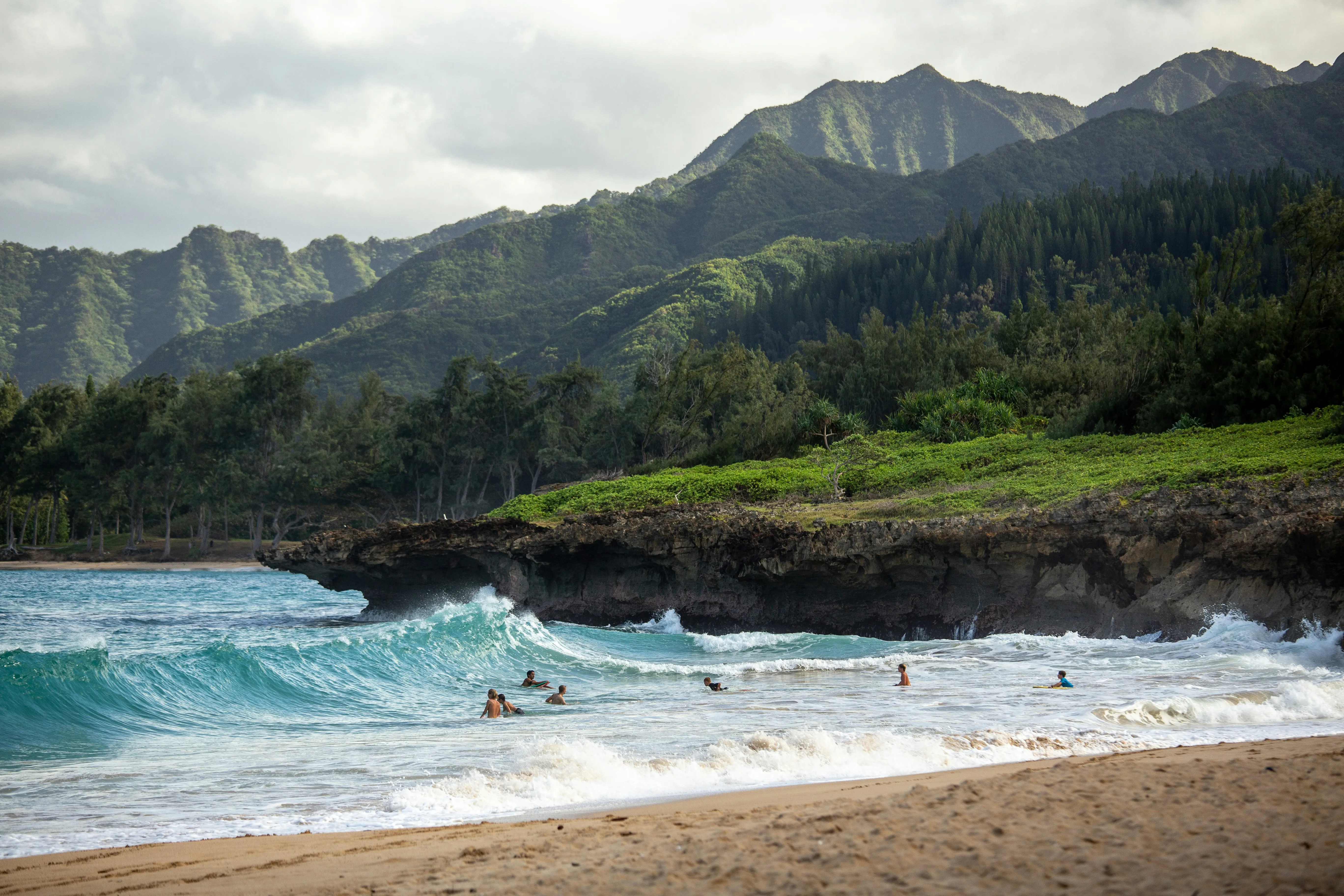 Baigneurs dans les vagues turquoise d'une plage d'Oahu, crêtes vertes des monts Koolau en arrière-plan