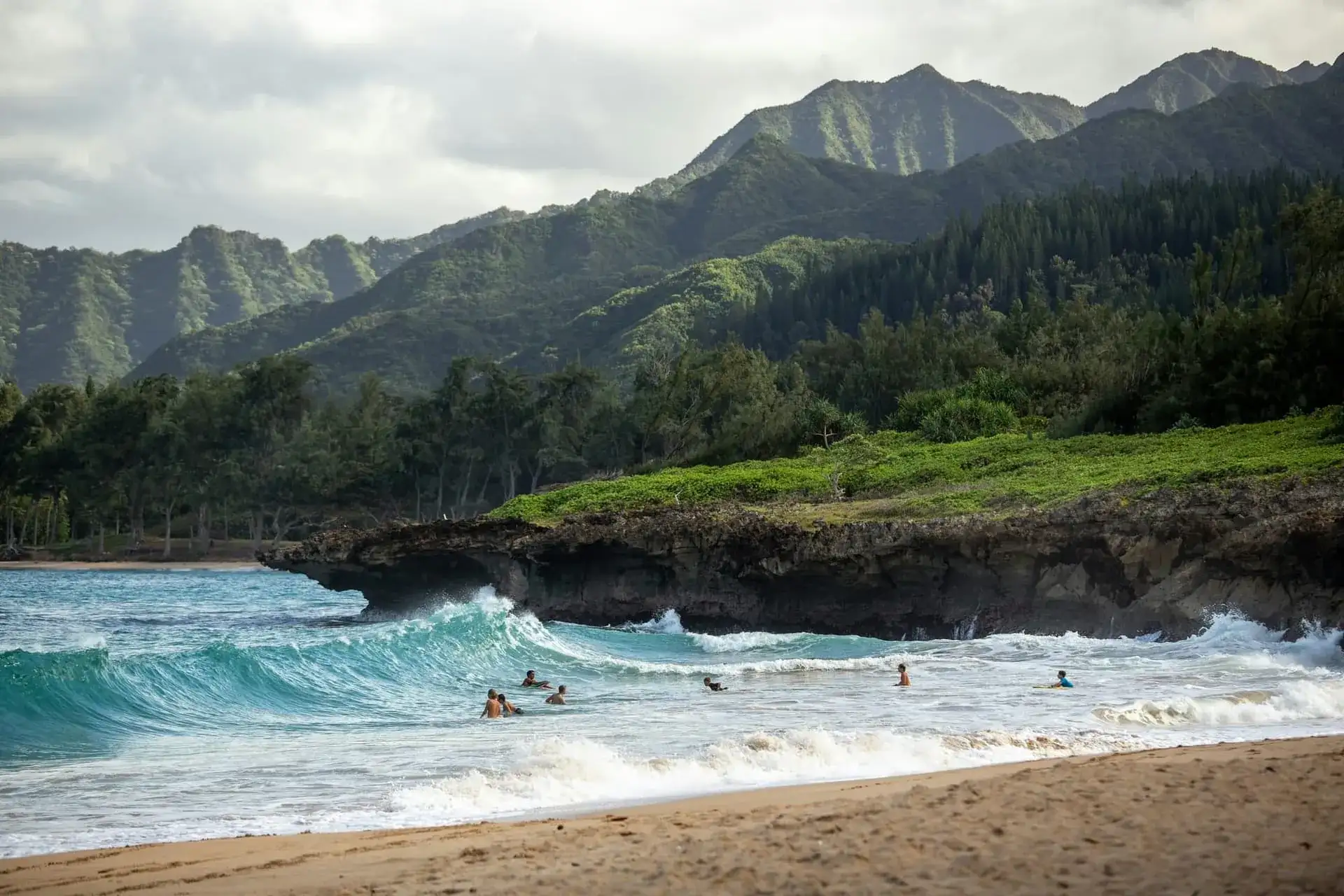 Baigneurs dans les vagues turquoise d'une plage d'Oahu, crêtes vertes des monts Koolau en arrière-plan