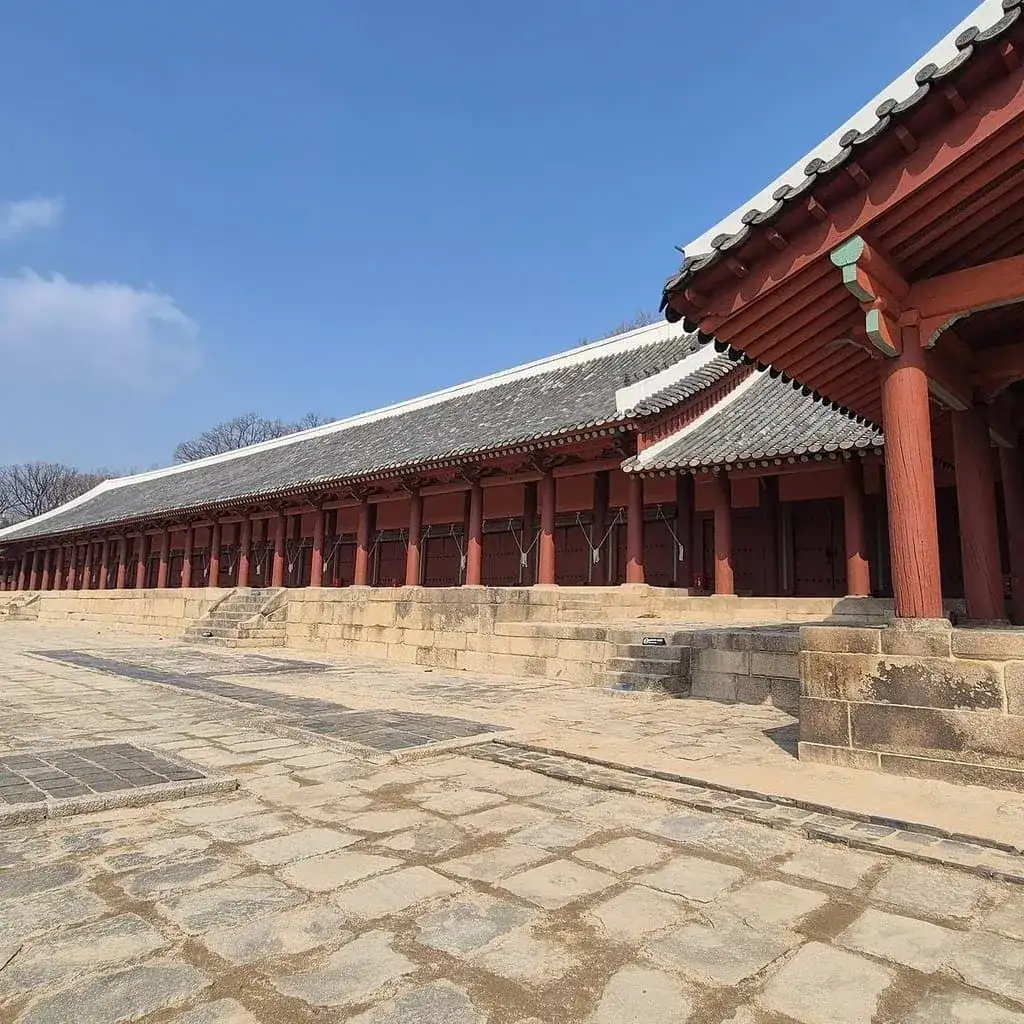 Le long hall de bois aux colonnes rouges du sanctuaire de Jongmyo et son parvis de pierre