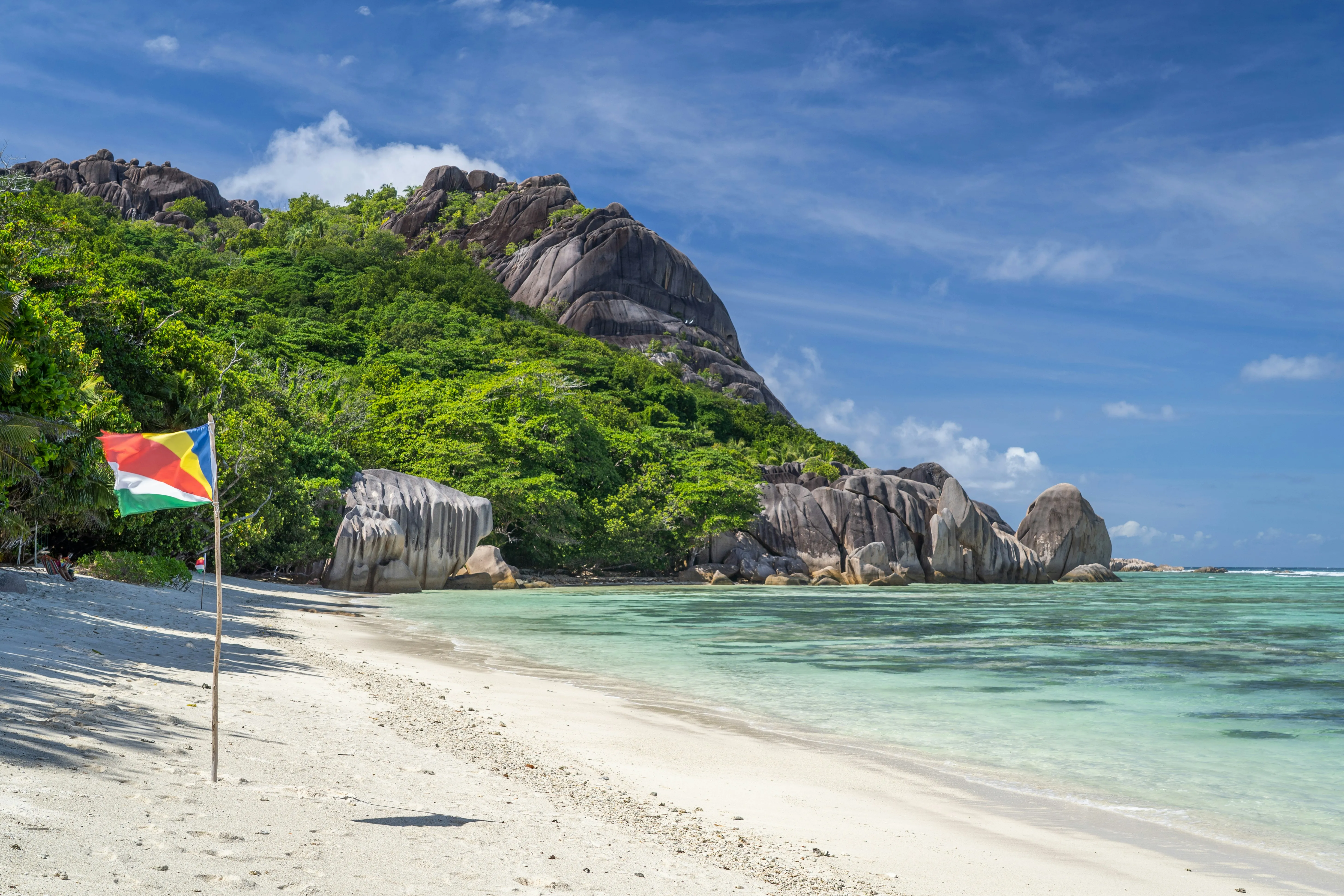 Plage de sable blanc et blocs de granit d'Anse Source d'Argent, drapeau seychellois planté face au lagon